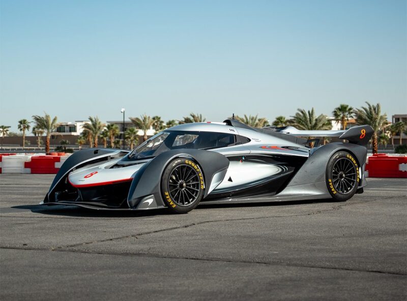 A sleek, black and silver McLaren Solus GT with red accents is parked on a private track at The Thermal Club, surrounded by palm trees and buildings under a clear blue sky.