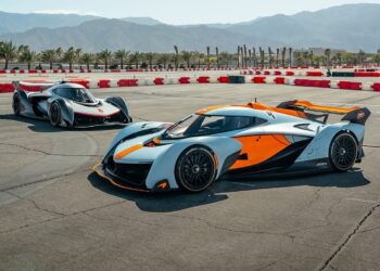 Two high-performance race cars, including a McLaren Solus GT, with aerodynamic designs and bold orange, black, and gray colors are parked at The Thermal Club racetrack—an exclusive venue known for private track days—with mountains in the background.
