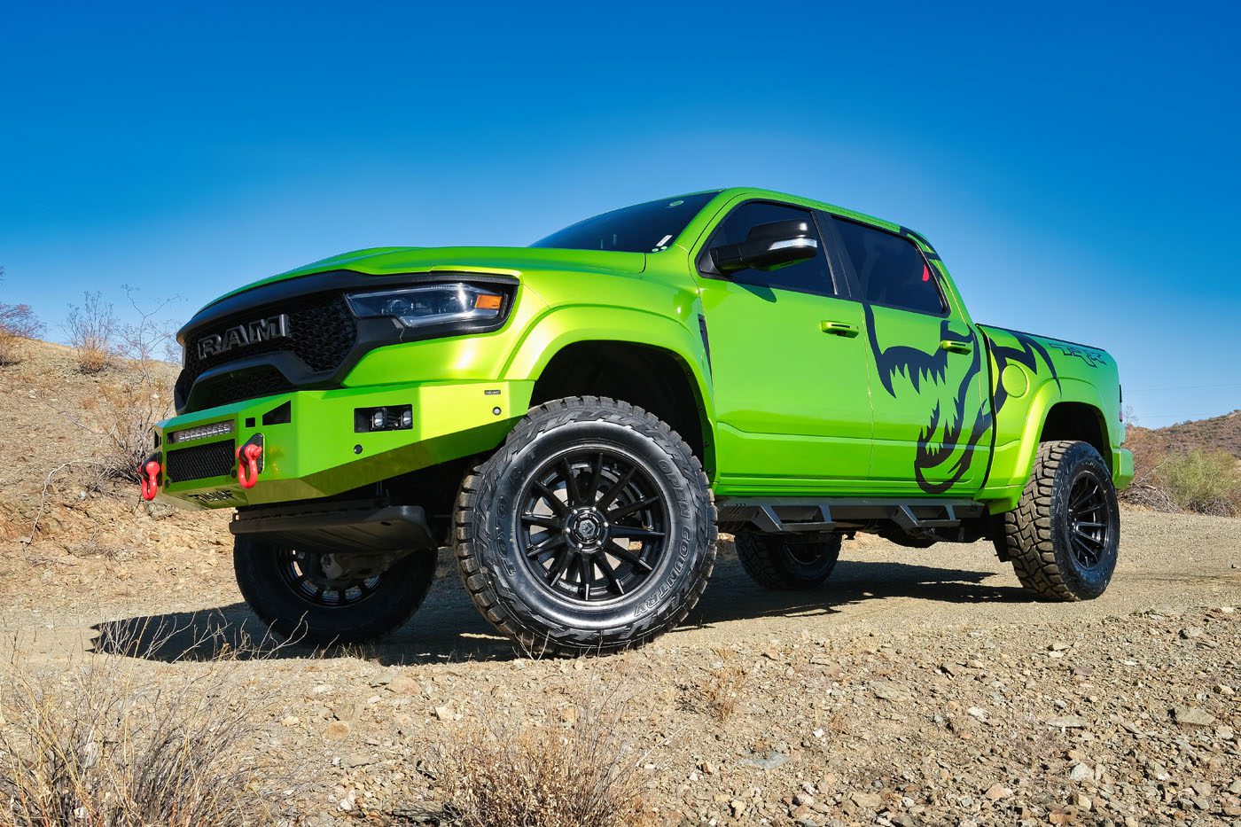 A bright green lifted truck with black graphic decals is parked on a rocky dirt road under a clear blue sky, showcasing the rugged style seen at America's original lifted truck dealer.