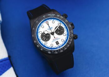 A TUDOR Black Bay Chrono watch with a white and blue dial, black subdials, black bezel, and black strap is displayed on a blue surface—an eye-catching tribute to the Miami F1 spirit.
