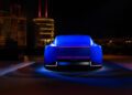 A blue luxury concept car is shown from the rear at night, illuminated by accent lighting, with modern buildings and yachts in the background.