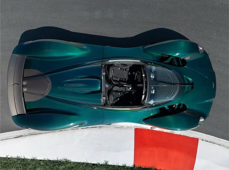 A Green Carbon convertible roadster is photographed from above, speeding along a racetrack near a red and white curb.