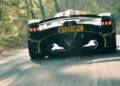 A green sports car with license plate "KY22 HPC" speeds down a forest road, sparks flying—Valkyrie Meets Cloverleaf On Aston Hill: Where It All Began 100 Years Ago.
