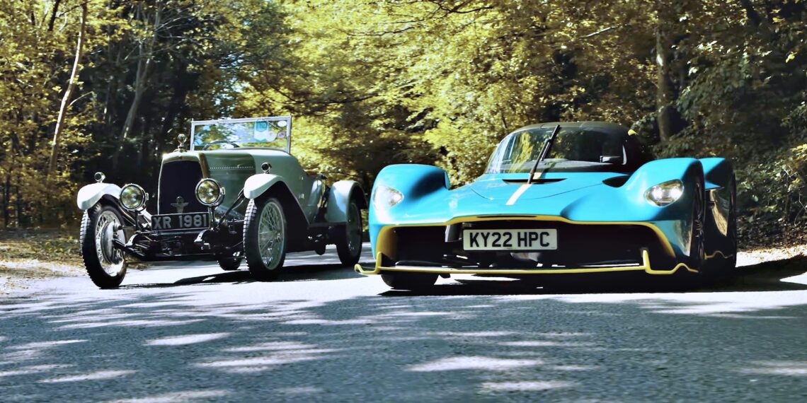 A vintage silver car and a modern blue sports car drive side by side on a tree-lined road in daylight—where Valkyrie Meets Cloverleaf On Aston Hill: Where It All Began 100 Years Ago.