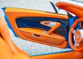 Close-up of an open car door featuring bright orange and blue interior details, visible steering wheel, and luxury car trim in this 1-of-1 Bugatti Veyron Grand Sport Vitesse.