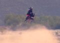 A person wearing a helmet rides a Volonaut Airbike—no wings, no rotors—above the ground, kicking up dust, with trees and mountains in the background. So how does the Airbike fly?.