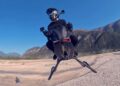 A person in black riding gear and helmet is airborne on a hoverbike above a rocky landscape with mountains in the background—No Wings No Rotors: So How Does The Volonaut Airbike Fly?.