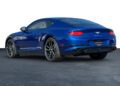 A blue Bentley coupe viewed from the rear left side, parked on a smooth surface with a plain white background.