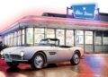 A classic silver convertible—How This BMW Went From Bold Gamble To Blue-Chip Classic—parks in front of a retro-style American diner, its neon lights shining beneath the iconic "Star Diner" sign.