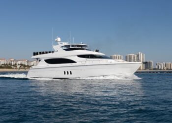 A large white yacht cruises on calm blue water with city buildings visible in the background under a clear sky, offering a true luxury yachts maritime experience.