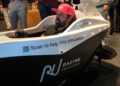 A man wearing a pink cap sits in a Racing Unleashed driving simulator at RAFA Racing Club Houston, with a QR code and "Scan to buy this simulator!" promotion on the side.