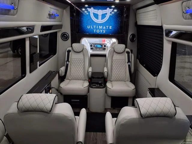 Luxury van interior with four leather seats, cupholders, flat-screen TV displaying the Ultimate Toys logo, and ambient lighting—experience comfort and style in custom luxury Sprinters.