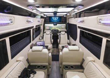Luxury van interior with cream leather seats, cup holders, screens, and ambient lighting in select Cruiser Models, all facing toward the driver's cockpit and dashboard monitor. Enjoy ultimate comfort—and explore June Savings on featured models.