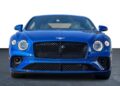 Front view of a blue Bentley Continental GT coupe parked on a dark surface with a white background.