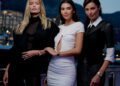 Three women posing together outdoors in evening attire, with buildings and mountains visible in the background at dusk, each wearing elegant Monaco Watches that highlight their sophisticated style.