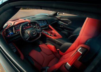 View of a modern 2026 Chevrolet sports car interior featuring red and black leather seats, digital dashboard, and a steering wheel with a Corvette logo.
