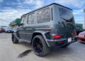 A gray Mercedes-AMG G 63 SUV is parked in a lot, viewed from the rear left side, with large black wheels and tinted windows under a partly cloudy sky—this impressive BRABUS-tuned vehicle is now for sale.