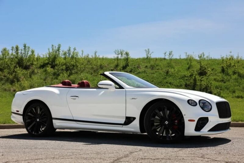 A white convertible luxury car with a black grille and black wheels is parked on a paved surface, surrounded by green grass and trees under a clear sky—perfect for top car listings or anyone seeking a luxury car for sale.