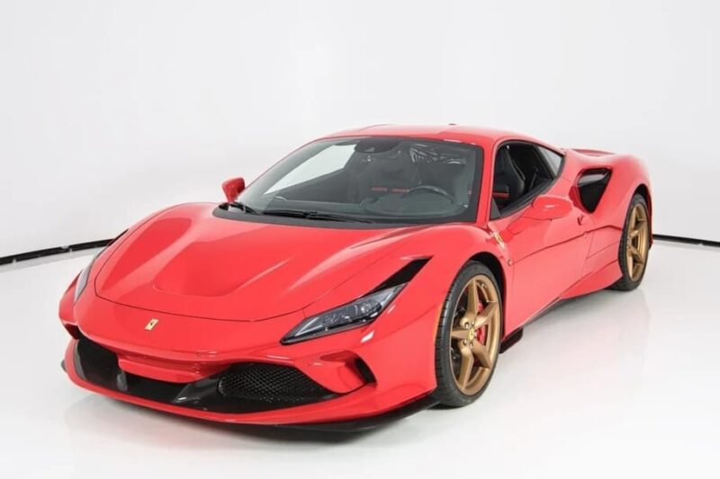 A red Ferrari sports car with bronze wheels is parked in a white studio setting, positioned at an angle to show the front and side—an exceptional exotic car for sale featured in top car listings.