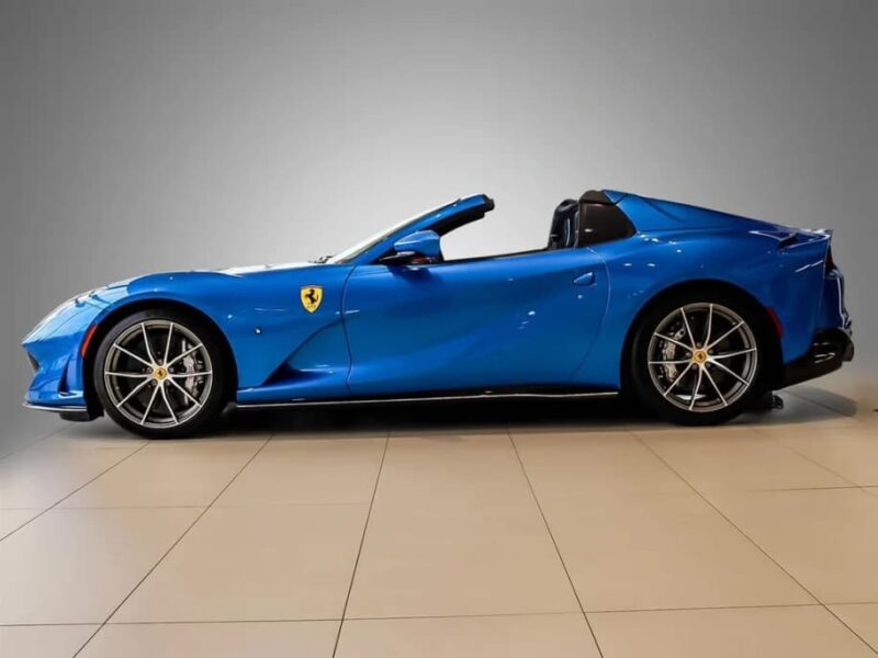A blue Ferrari convertible luxury car is shown in a side profile view against a gray background, parked on a tiled floor.