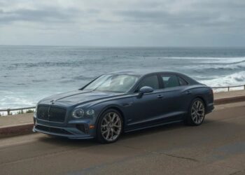 A blue luxury car sedan parked on a coastal road, with the ocean and a cloudy sky in the background—an ideal choice for those browsing exotic car for sale listings.