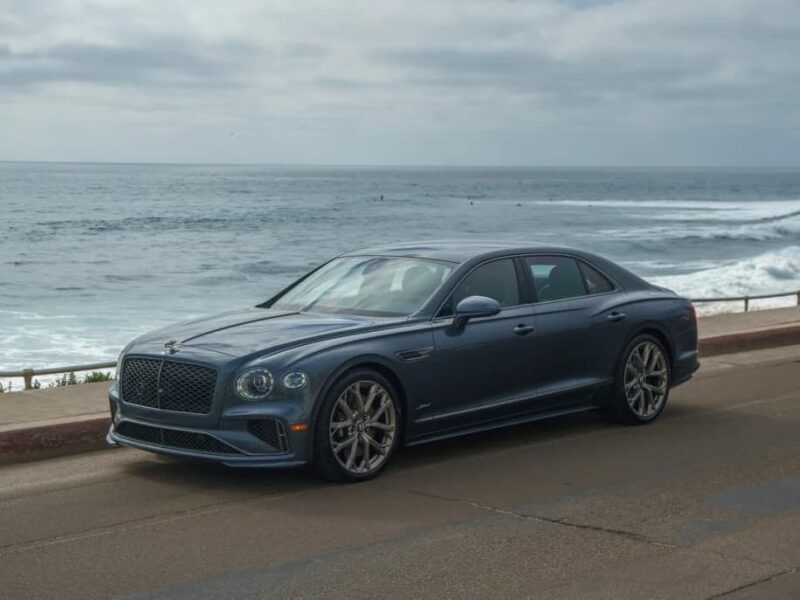 A blue luxury car sedan parked on a coastal road, with the ocean and a cloudy sky in the background—an ideal choice for those browsing exotic car for sale listings.