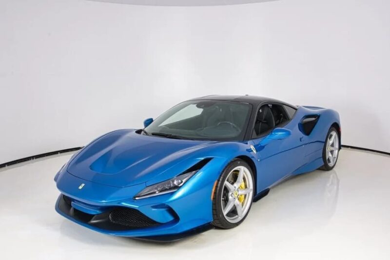 A blue Ferrari luxury car with a black roof is parked in a white, curved photo studio.