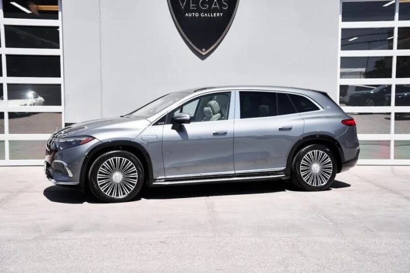 A silver Mercedes-Benz luxury car is parked in front of a building with large windows and a sign that reads "Vegas Auto Gallery.