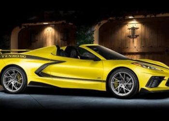A yellow convertible muscle car with "Yenko SC" on the side, built by Specialty Vehicle Engineering, is parked in front of wooden double doors under outdoor lighting.