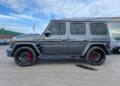 A gray Mercedes-Benz G-Class SUV with black rims and red brake calipers is parked outside on a cloudy day.