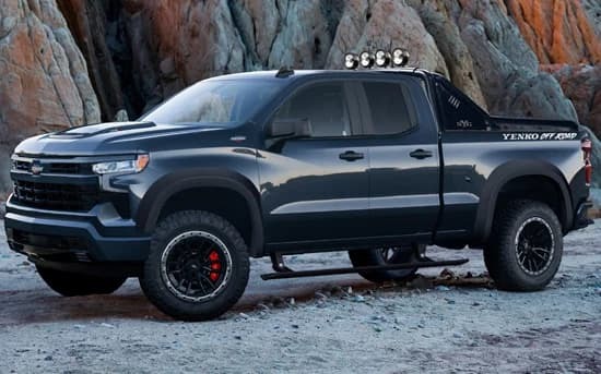 A black pickup truck from Specialty Vehicle Engineering with off-road tires and roof lights is parked on a rocky terrain with cliffs in the background.