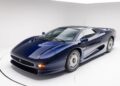 A Le Mans Blue Jaguar XJ220 sports car is parked in a white studio, viewed from the front left corner.