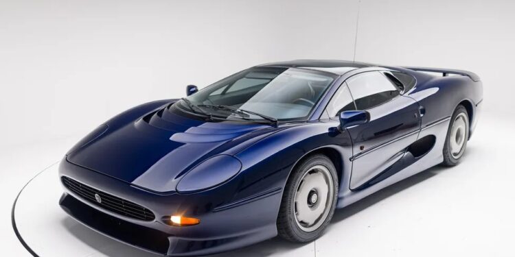 A Le Mans Blue Jaguar XJ220 sports car is parked in a white studio, viewed from the front left corner.