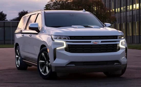 A white Chevrolet SUV, inspired by Specialty Vehicle Engineering's legacy with muscle cars, is parked outdoors near a modern glass building at dusk.