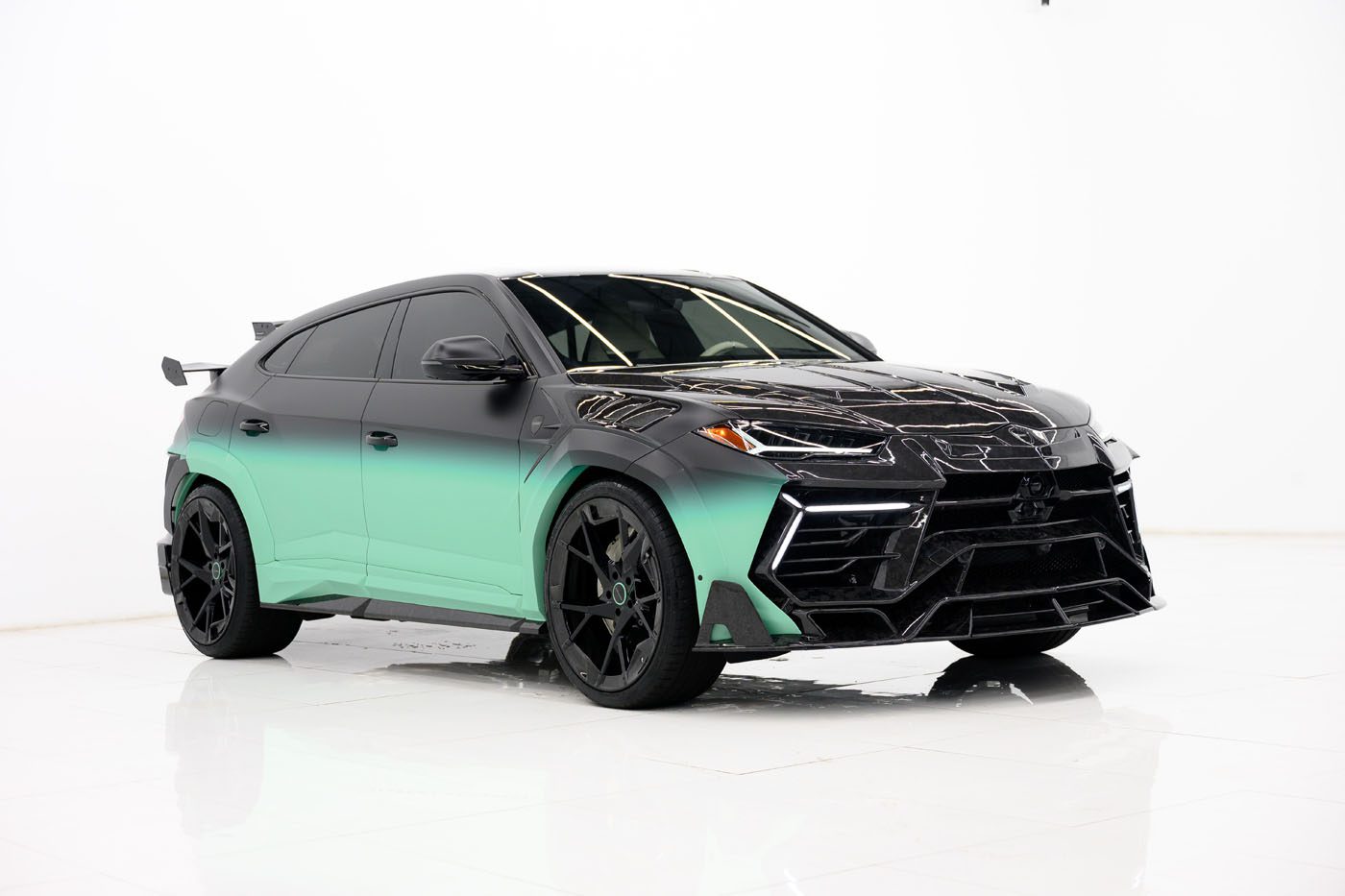 A black and green Lamborghini Urus SUV with tinted windows and custom black wheels, showcased in a white studio, rivals any 2025 Cullinan Limited Spec in style and presence.