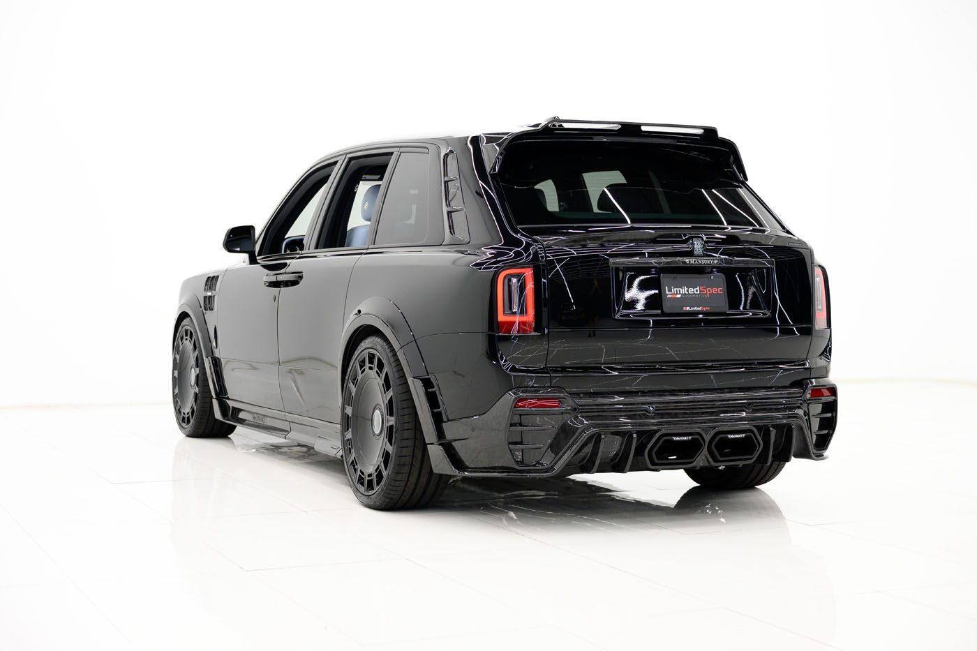 A black 2025 Cullinan Limited Spec luxury SUV with custom rims and tinted windows is parked indoors on a shiny white floor, viewed from the rear left side.
