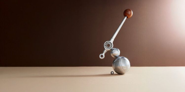 A metallic abstract sculpture with spheres and a lever-like arm topped with a wooden ball, placed on a beige surface against a brown gradient background.