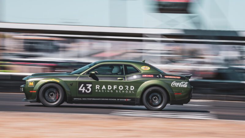 A green Dodge race car with the number 43 and Radford Racing School branding speeds on a race track, with blurred background indicating motion.