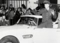 A man in military uniform sits on the door of a classic car, gesturing with raised arms, as a crowd watches and takes photos—capturing the story of how this BMW went from bold gamble to blue-chip classic.