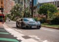 A black Rimac Nevera luxury sports car is parked on a street lined with palm trees and modern buildings, evoking the glamour of the Monaco Grand Prix in an urban setting.