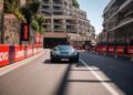 A black Rimac Nevera speeds along a city street circuit lined with Lenovo advertisements and modern buildings, reminiscent of the excitement at the Monaco Grand Prix.