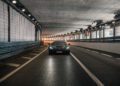 A black Rimac Nevera is driving through a well-lit tunnel with tiled walls and overhead lights, evoking the excitement of the Monaco Grand Prix.