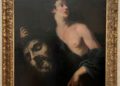 A fine art framed painting of a person holding a large severed head, with dramatic lighting highlighting their partially draped figure.