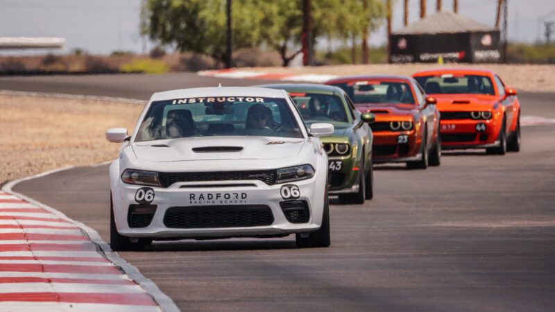 A white instructor car leads a line of colorful sports cars around a curve on a racetrack at the Radford Racing School.