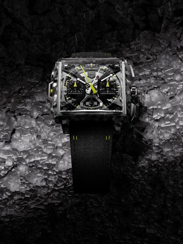 A square-faced black TAG Heuer wristwatch with neon yellow accents and a fabric strap is displayed against a textured, dark background, evoking the bold spirit of Monaco Watches.