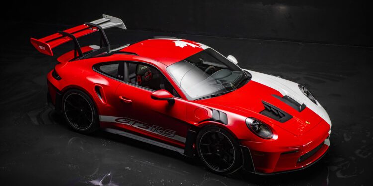 A red and white 911 GT3 RS with a large rear wing and a maple leaf design on the roof, photographed in a dark studio setting, reminiscent of models showcased at the Porsche Experience Center.