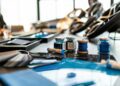 Close-up of a table with blue paint jars, a spool of blue thread, color swatches, and design materials arranged in a well-lit workspace, evoking the luxury experience of configuring your own Bugatti Tourbillon.