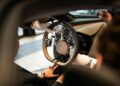 A person wearing white gloves presents the steering wheel and dashboard of a luxury Bugatti Tourbillon to two seated individuals, highlighting the experience of configuring their dream car.