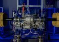 A Bugatti Tourbillon differential mounted on a test bench in a laboratory, connected to equipment and surrounded by blue-lit electronic devices and wiring, highlights the engineering behind the groundbreaking Hybrid V16.