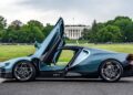 A blue Bugatti sports car with its doors open upwards is parked on a road near the White House in Washington D.C., looking like it just left a luxury showroom, framed by green trees in the background.